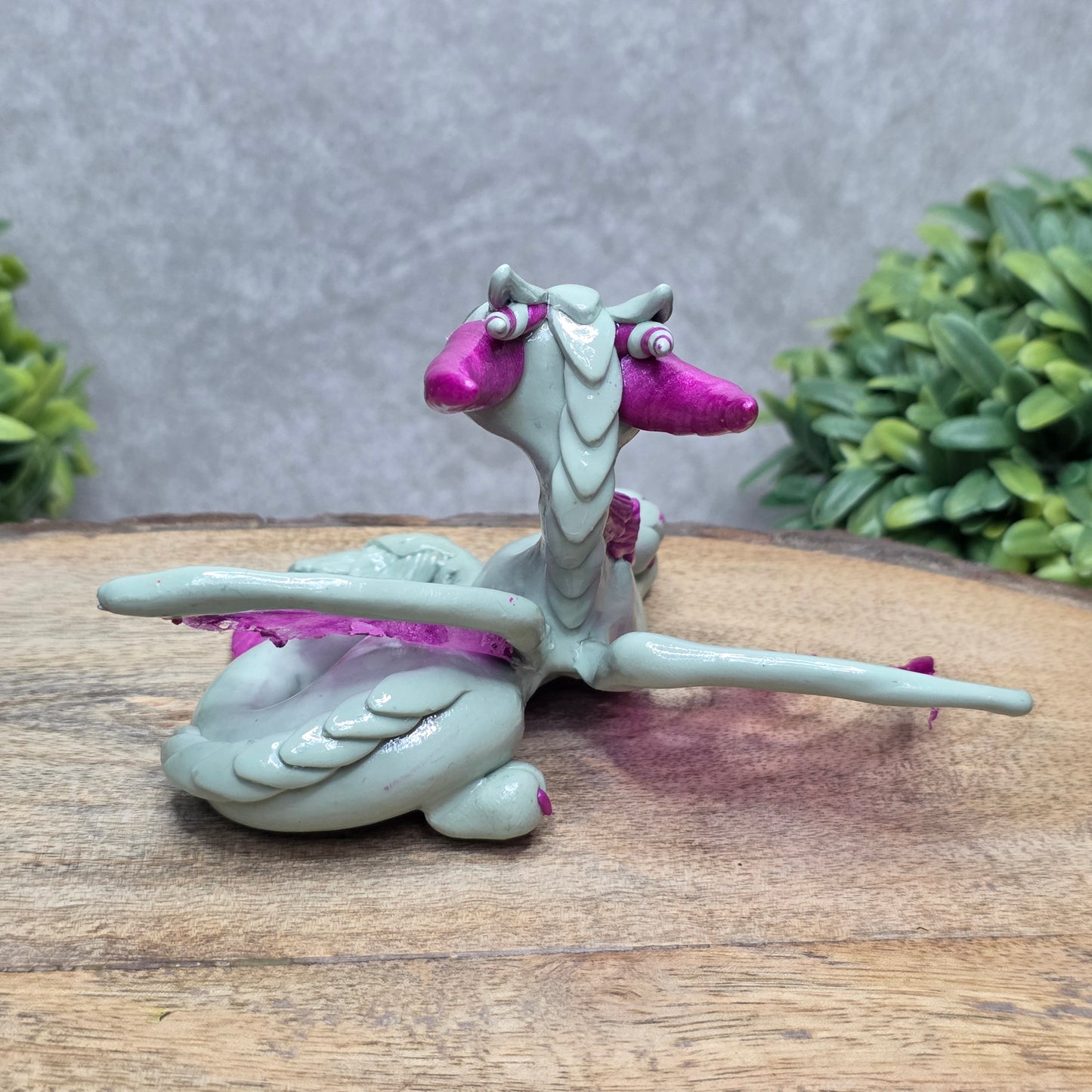 Back view of a clay dragon against a wood surface with greenery.