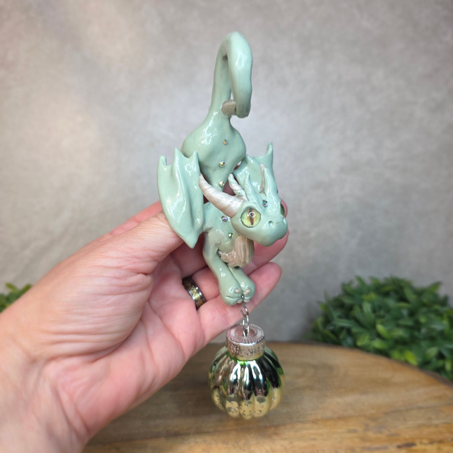Hand holding a small aqua dragon with glass ornament against a blurred background