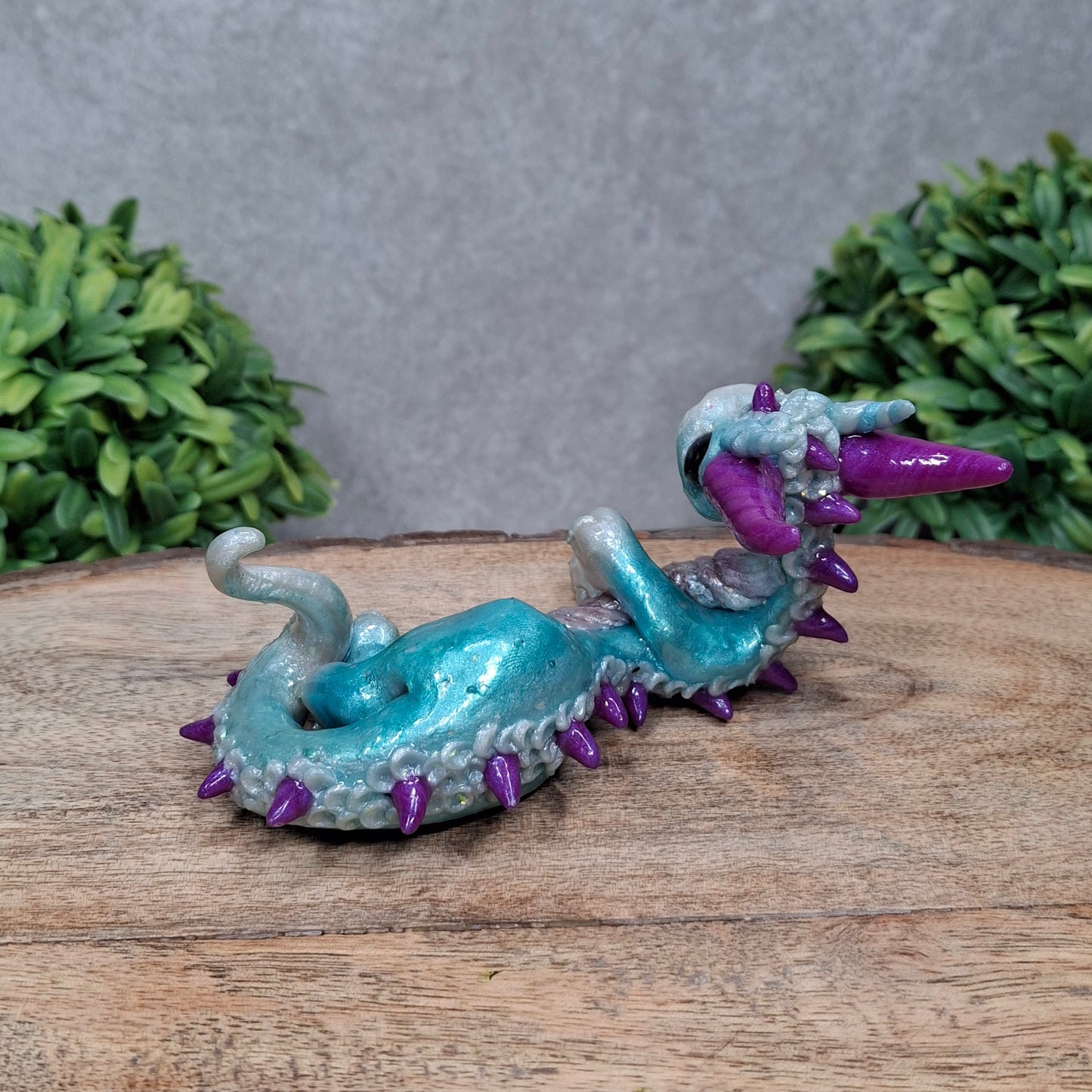 A clay dragon against a wood background with greenery