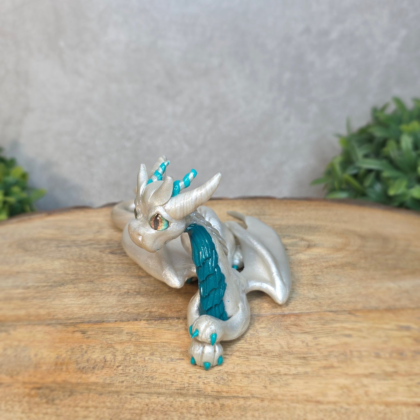 A white and teal clay dragon against a blurred wood surface