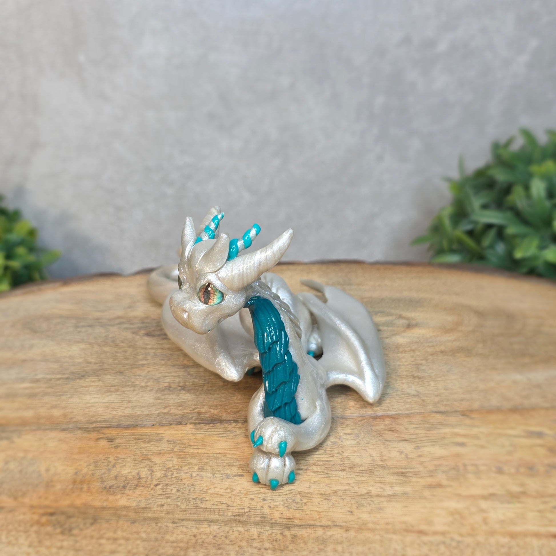 A white and teal clay dragon against a blurred wood surface