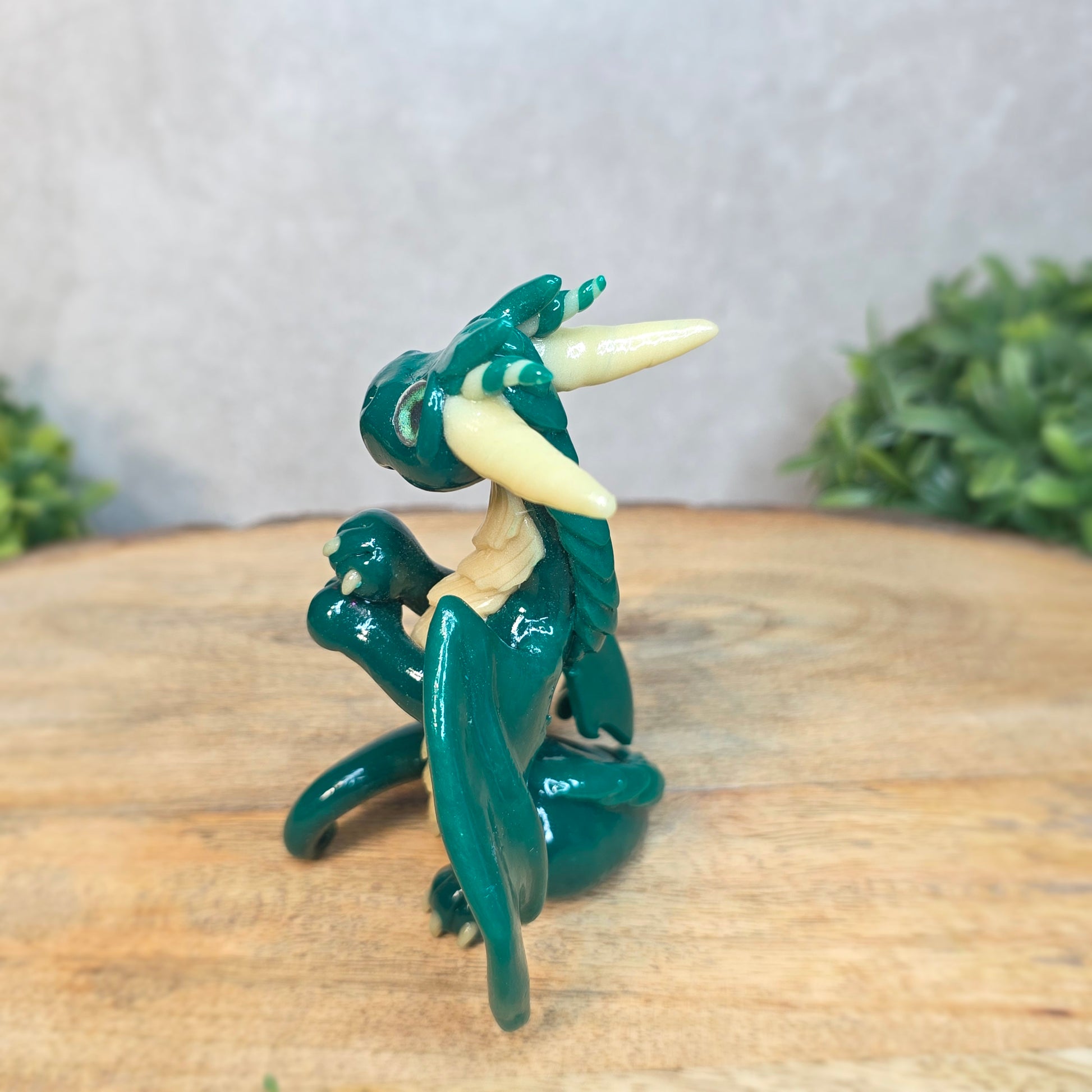 A green and cream clay dragon against a blurred wood surface