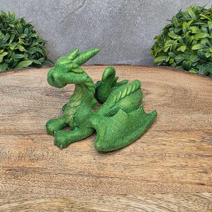 A flocked clay dragon sculpture on a wood surface with greenery.