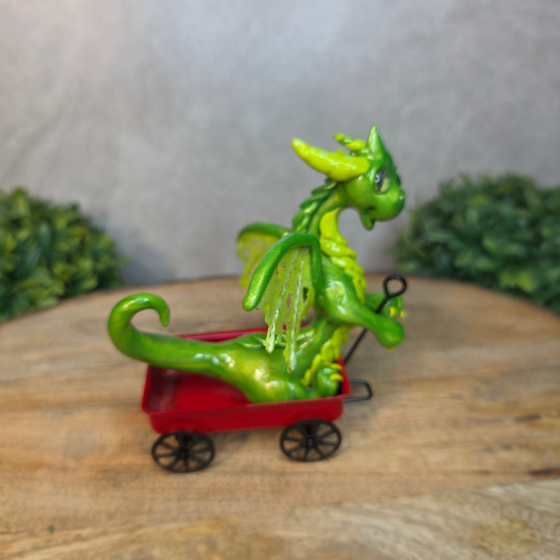 A green clay dragon in a red wagon on a wood surface