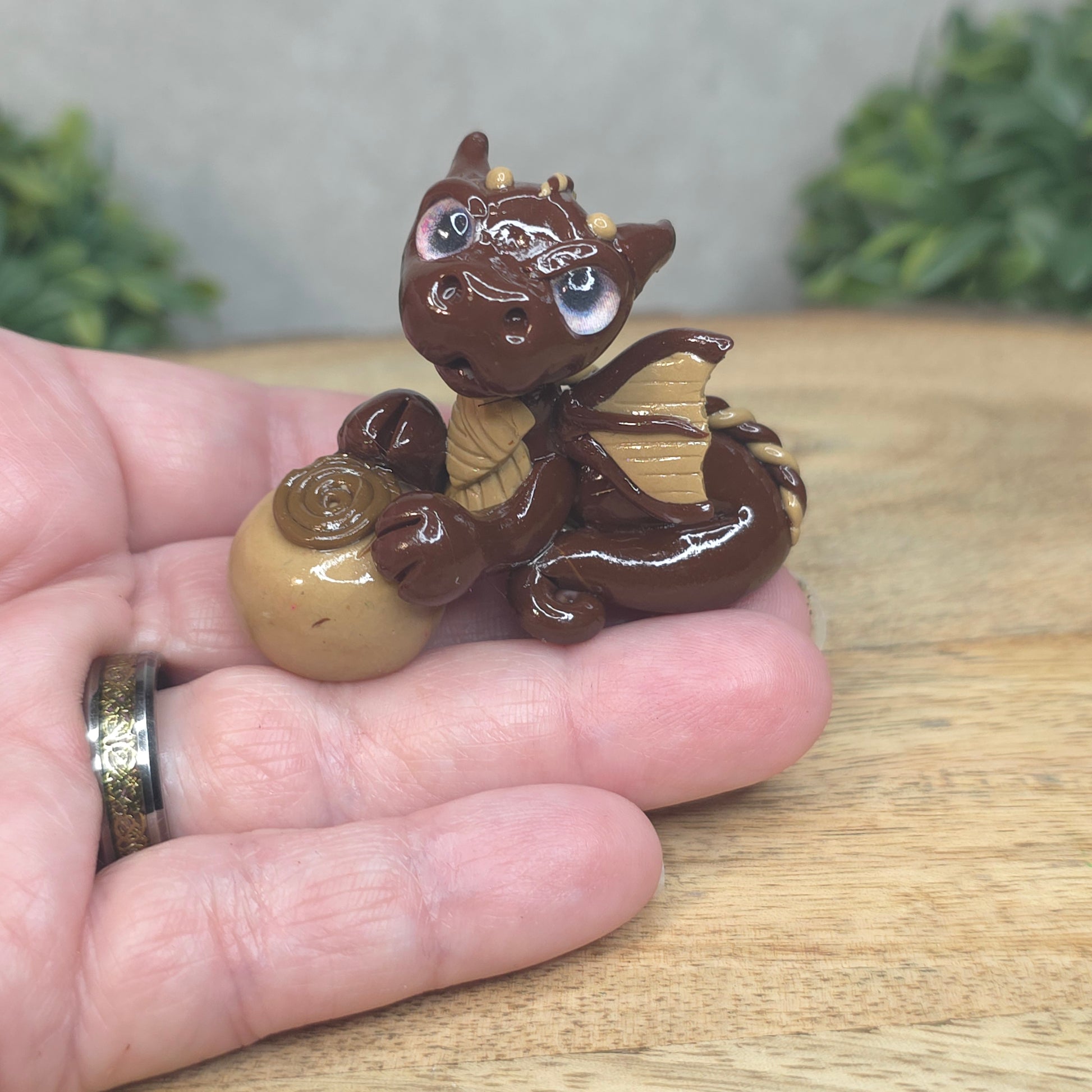 A hand holding a baby polymer clay dragon with a chocolate truffle against a blurred background