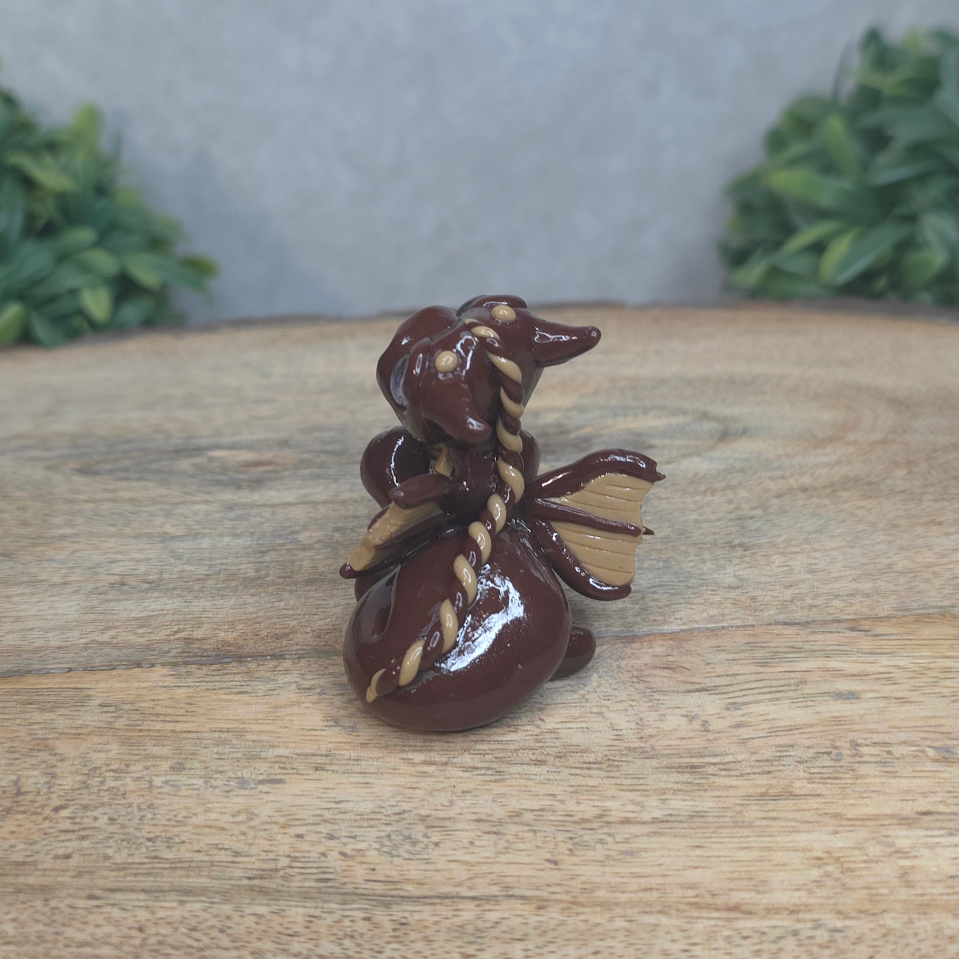A baby polymer clay dragon with a chocolate truffle against a blurred background