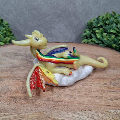 A yellow dragon with rainbow accents on a cloud sitting against a wood surface with greenery