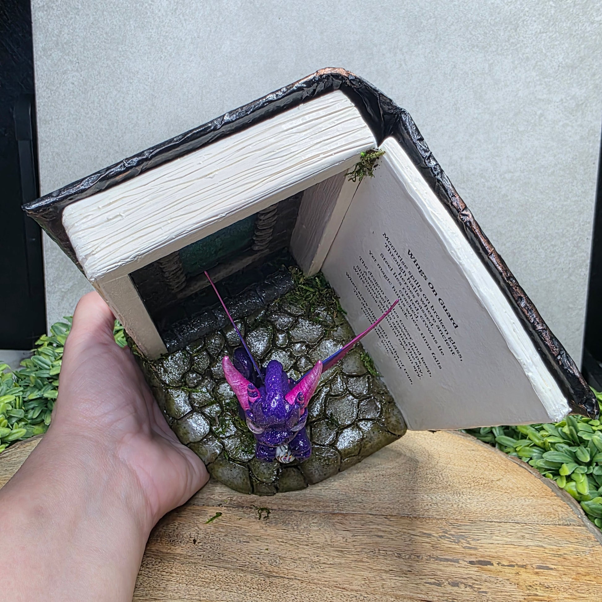 Book nook with fairy dragon on a wood surface with greenery