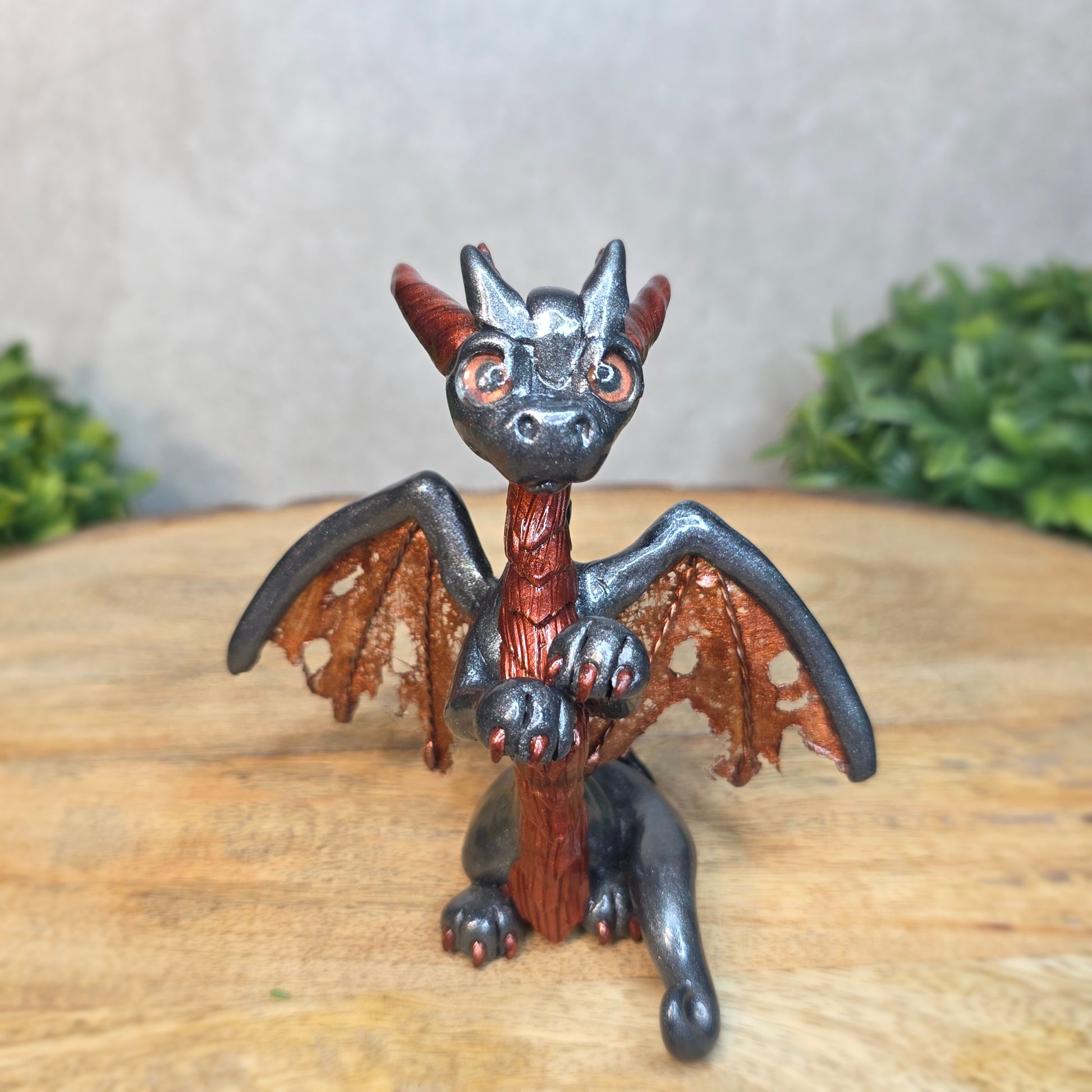 A graphite and bronze clay dragon against a blurred wood surface