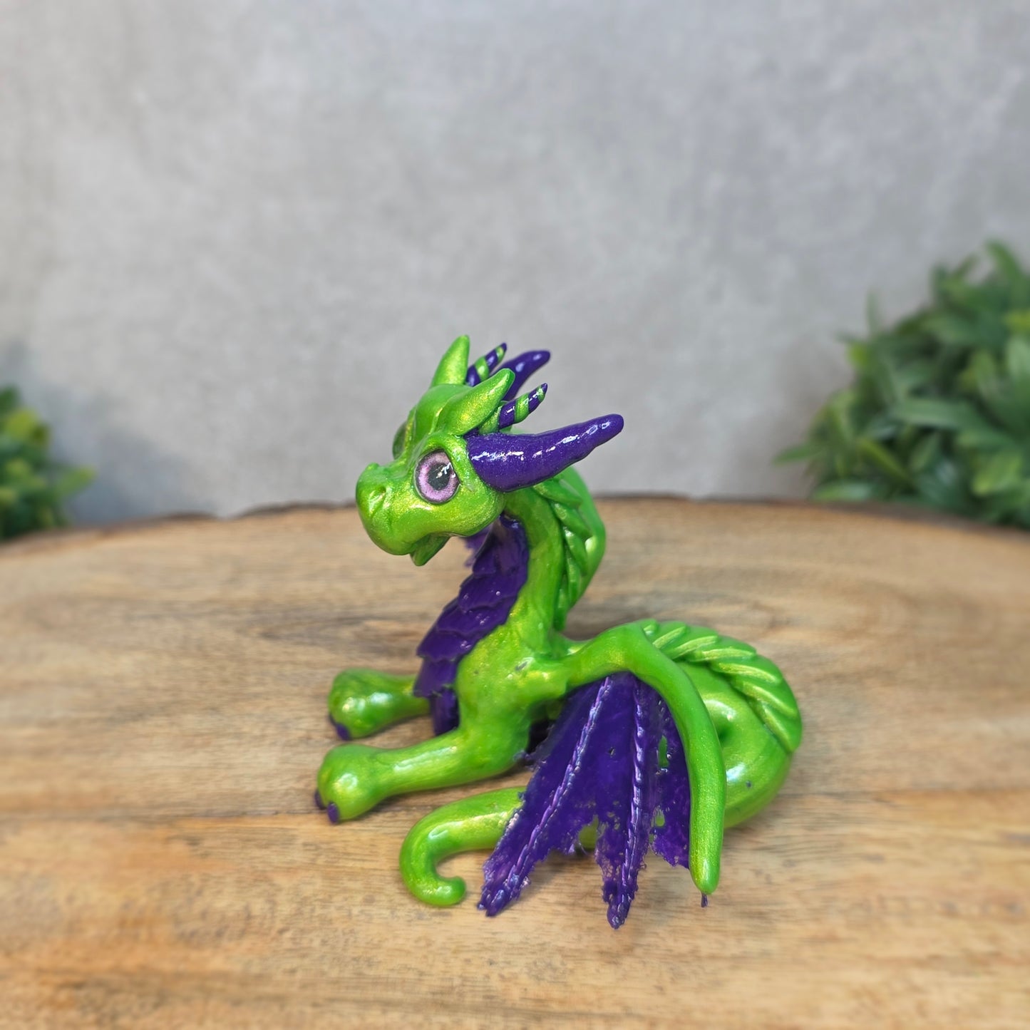 A green and purple clay dragon against a blurred wood surface