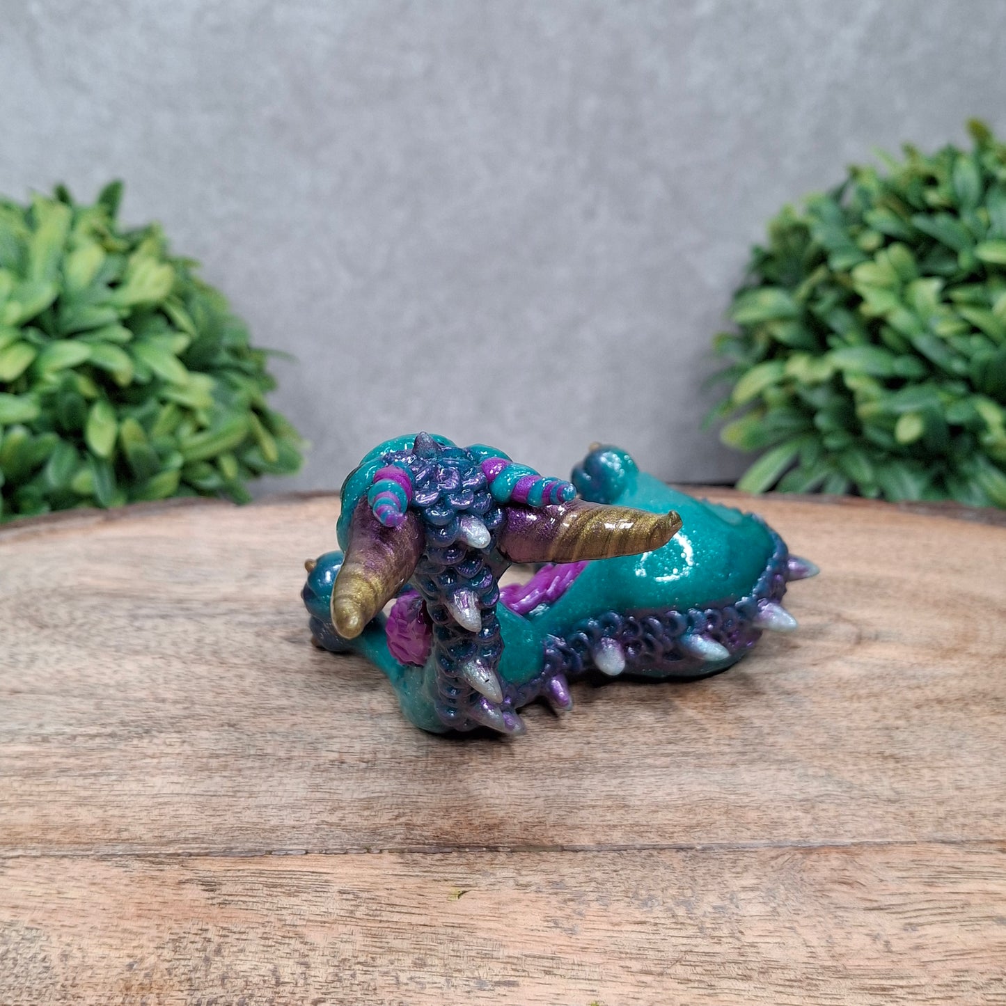 A  clay dragon against a wood background with greenery