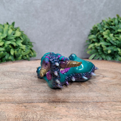 A  clay dragon against a wood background with greenery