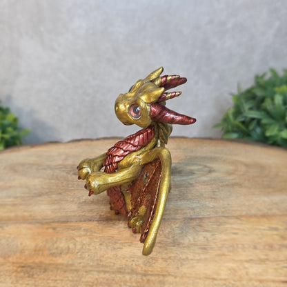 A gold and bronze clay dragon against a blurred wood surface