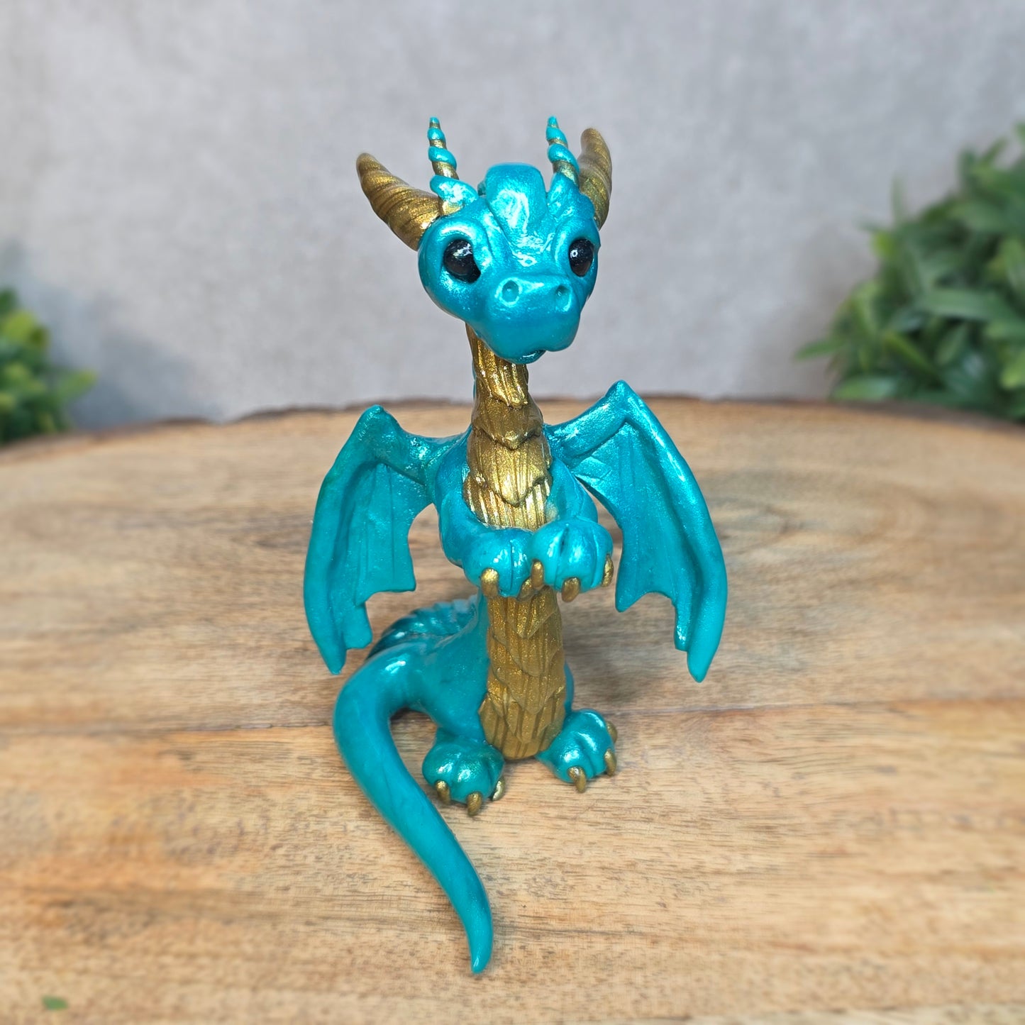 A teal and gold clay dragon against a blurred wood surface