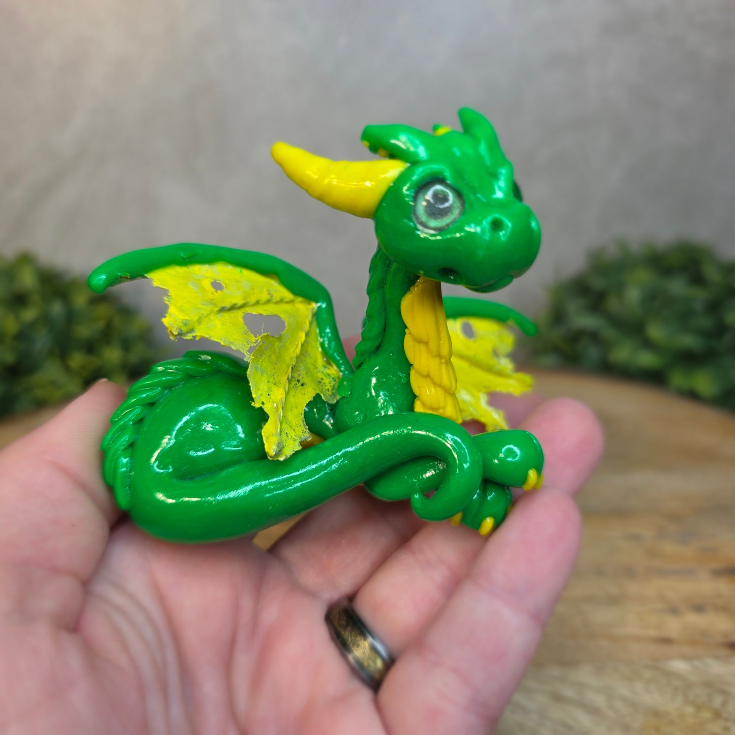 A hand holding a green and yellow dragon against a blurred wood surface