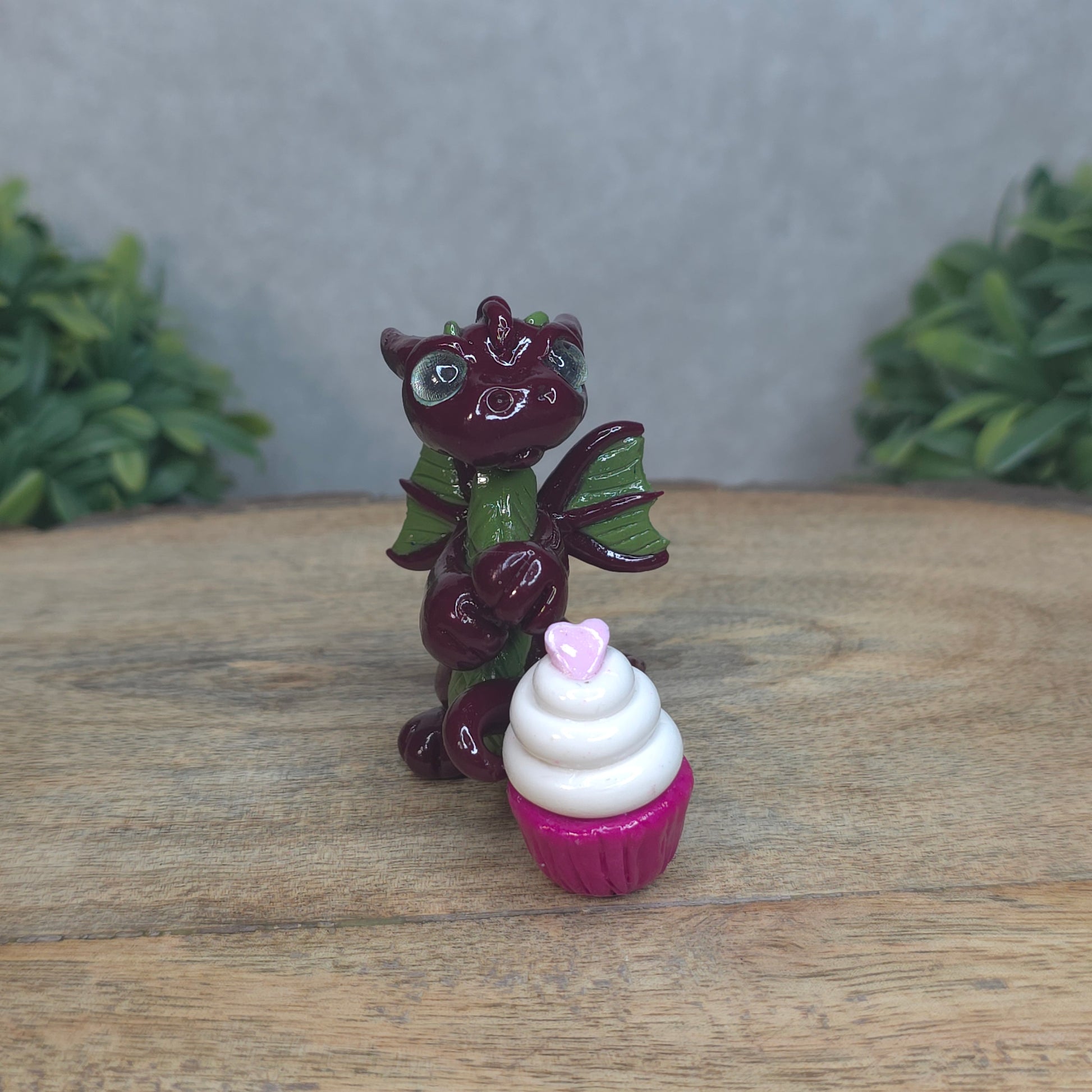 A baby polymer clay dragon with a cupcake against a blurred background