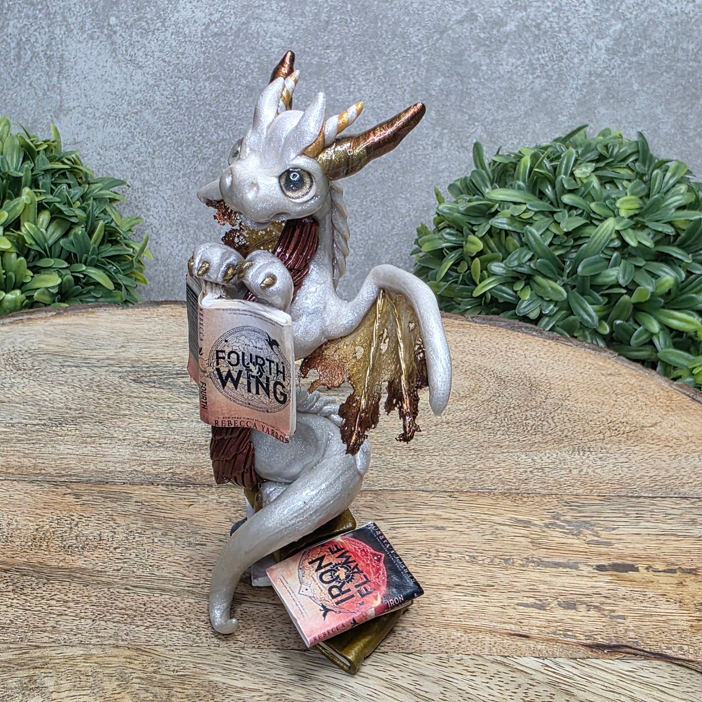 A dragon reading a book against a wood surface with greenery