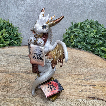 A dragon reading a book against a wood surface with greenery