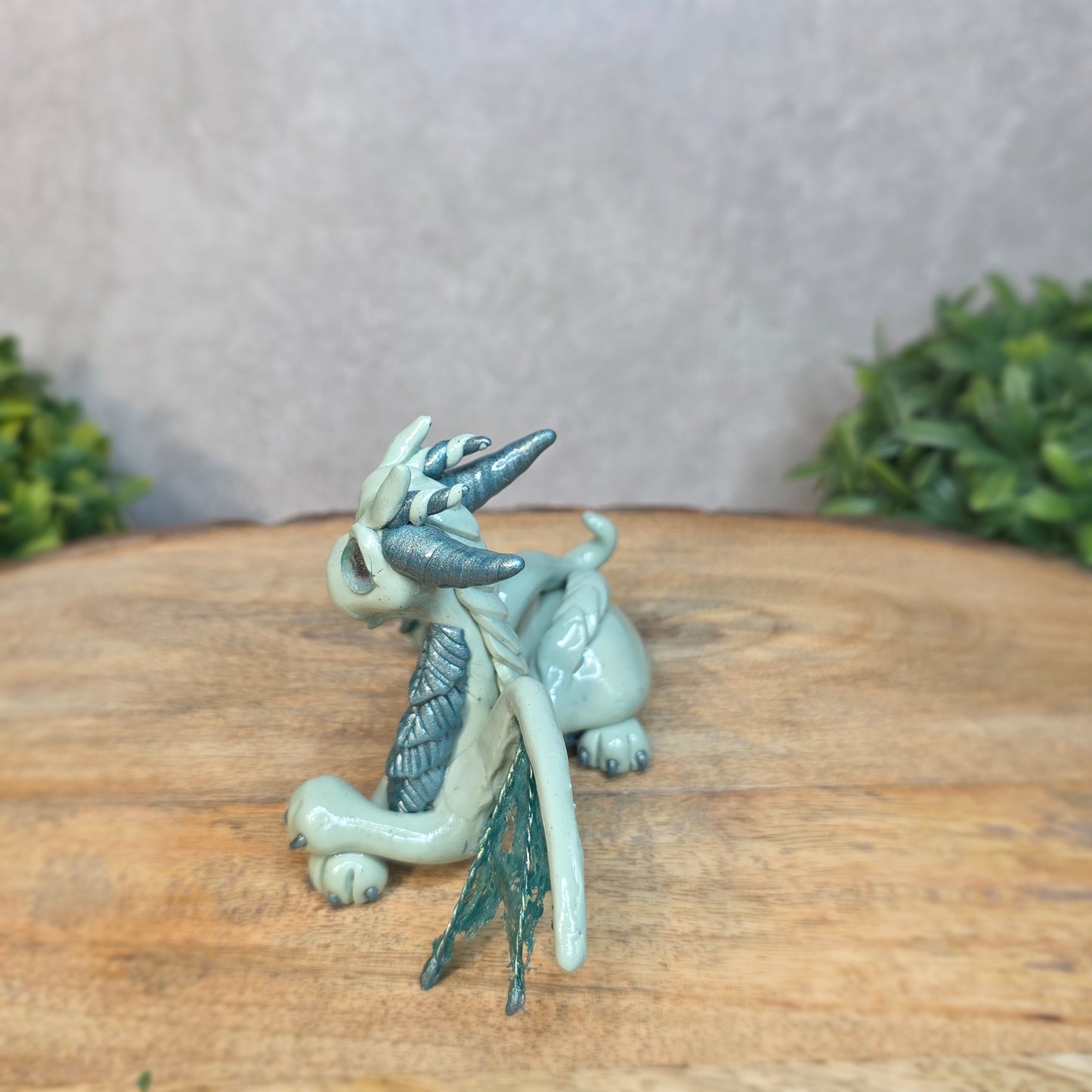 An aqua and turquoise clay dragon against a blurred wood surface