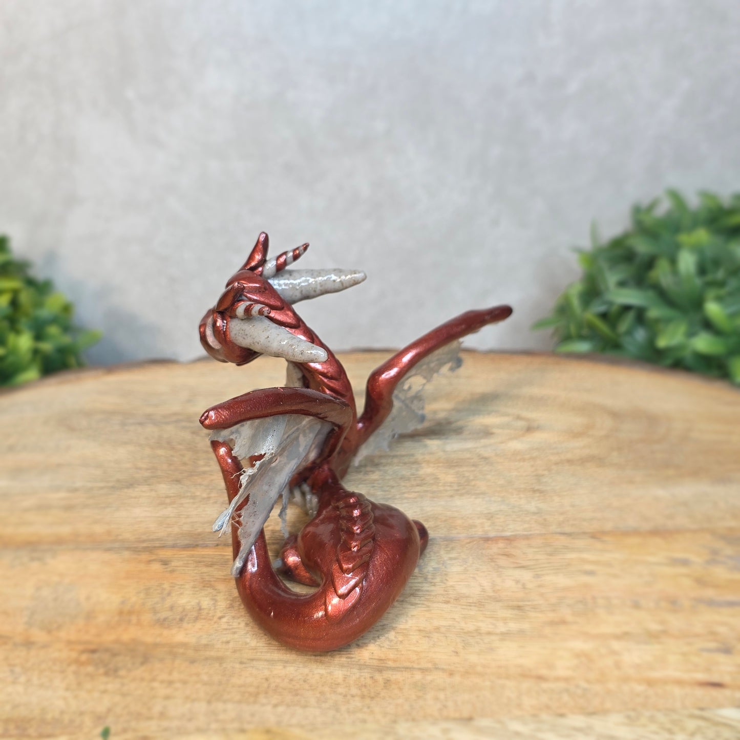 A bronze and gray clay dragon against a blurred wood surface