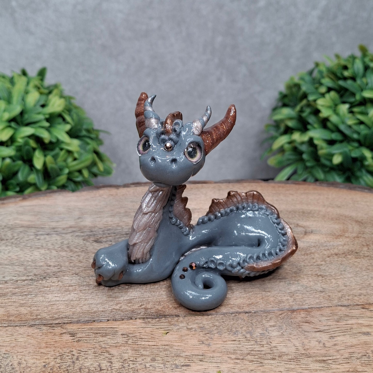 A clay dragon against a wood background with greenery