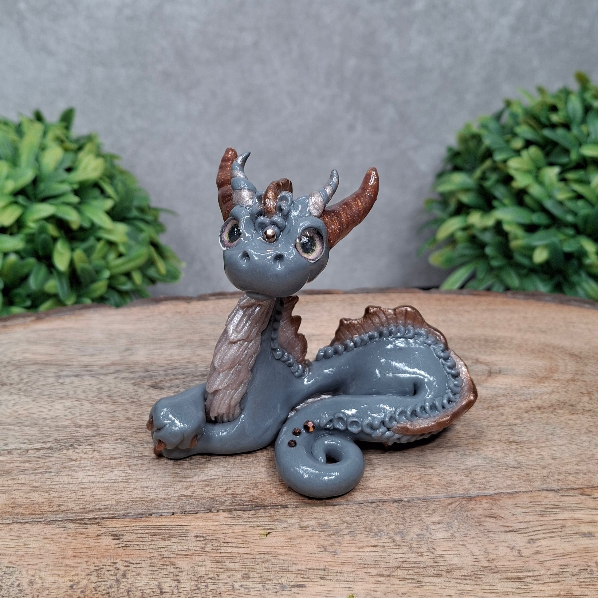 A clay dragon against a wood background with greenery