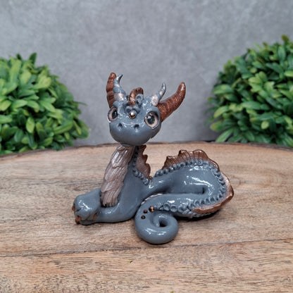 A clay dragon against a wood background with greenery