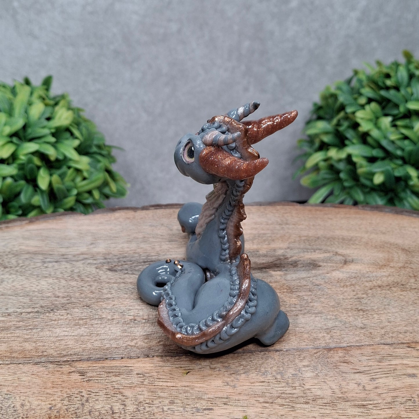 A clay dragon against a wood background with greenery