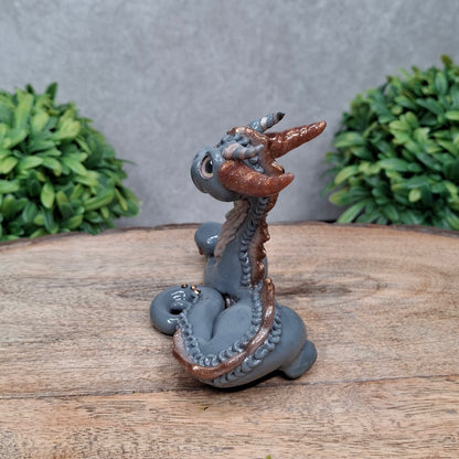 A clay dragon against a wood background with greenery