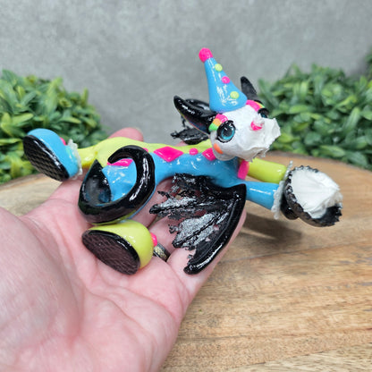 A hand holding a clown dragon with a cream pie on face