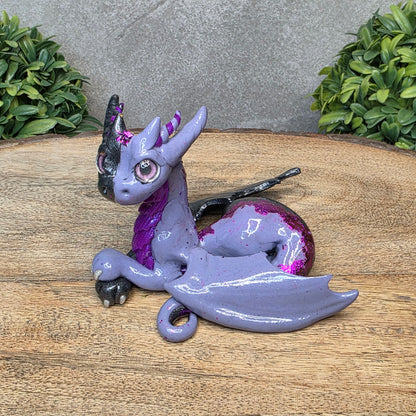 A 2 toned clay dragon sculpture on a wood surface with greenery.