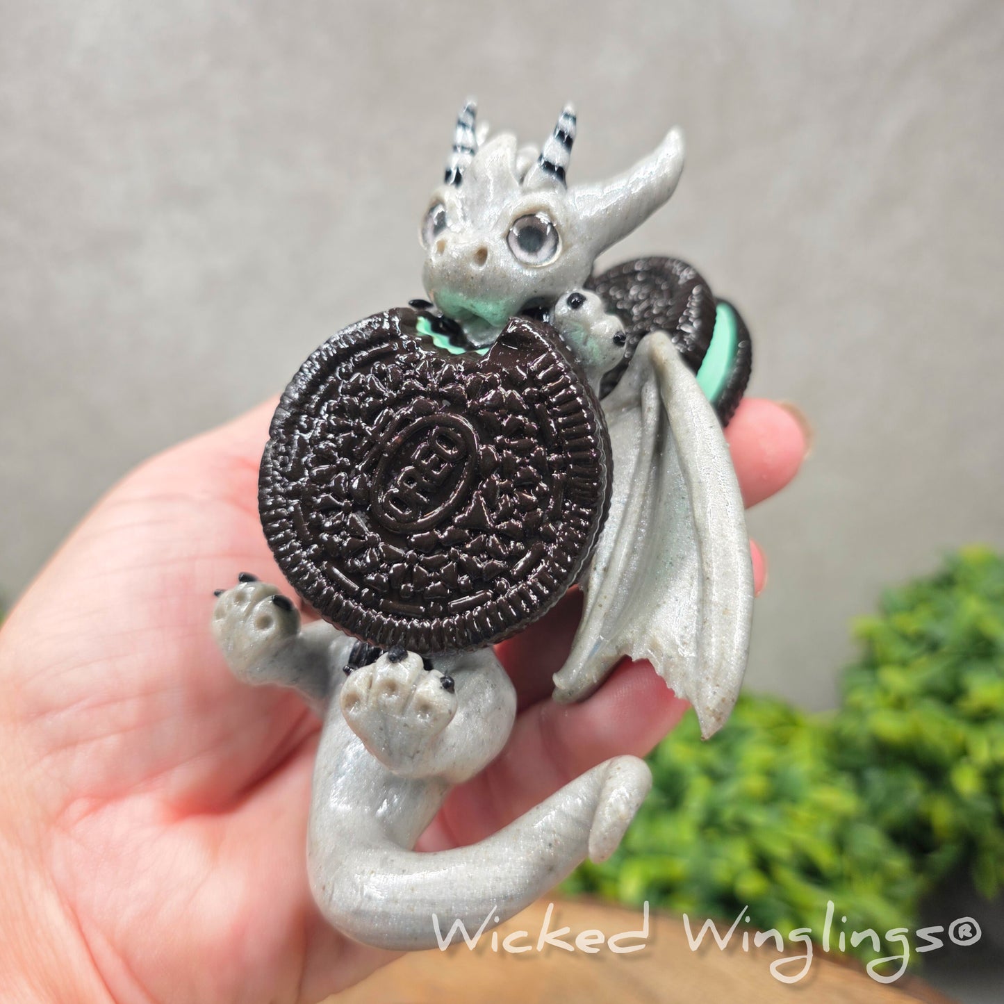 A hand holding a clay dragon with cookies with a Wicked Winglings® watermark.
