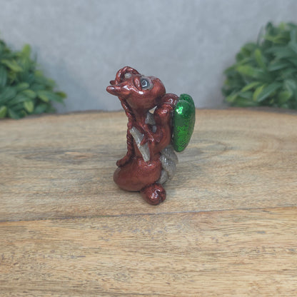 A baby polymer clay dragon with a green heart against a blurred background