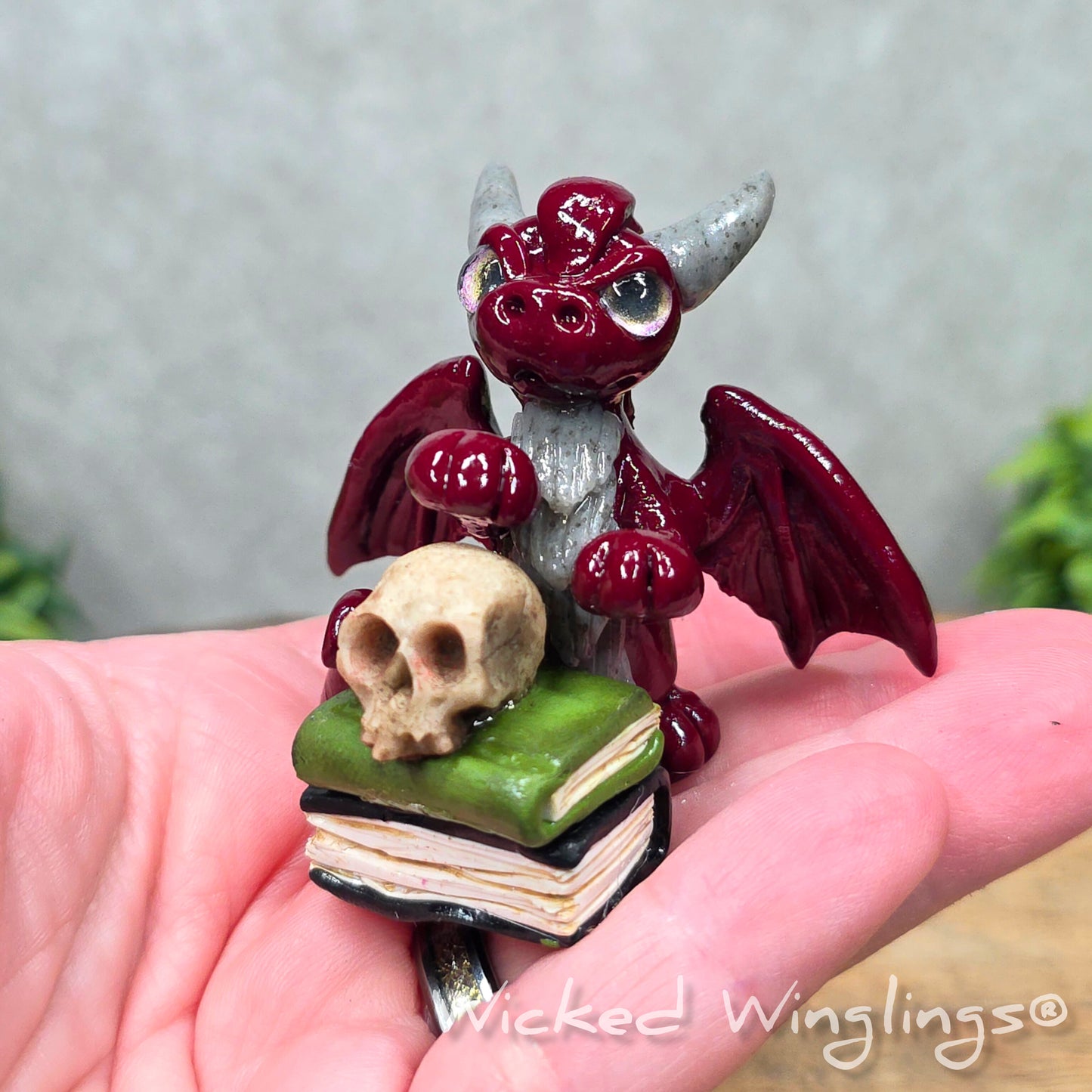 A hand holding a baby clay dragon with a skull and books