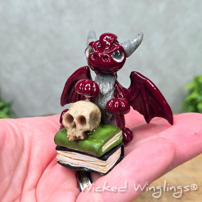 A hand holding a baby clay dragon with a skull and books