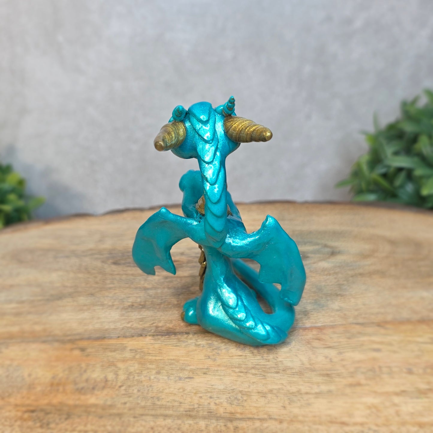 A teal and gold clay dragon against a blurred wood surface