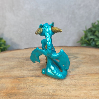 A teal and gold clay dragon against a blurred wood surface