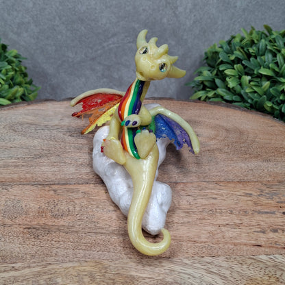 A yellow dragon with rainbow accents on a cloud sitting against a wood surface with greenery