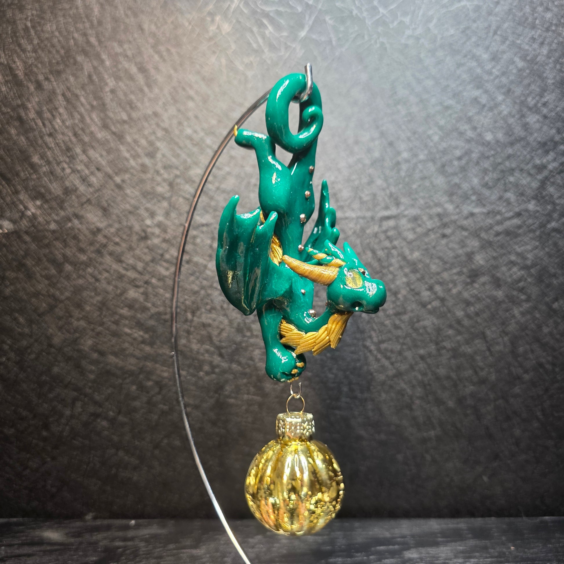 Clay green and gold dragon with a glass ornament hanging from an stand