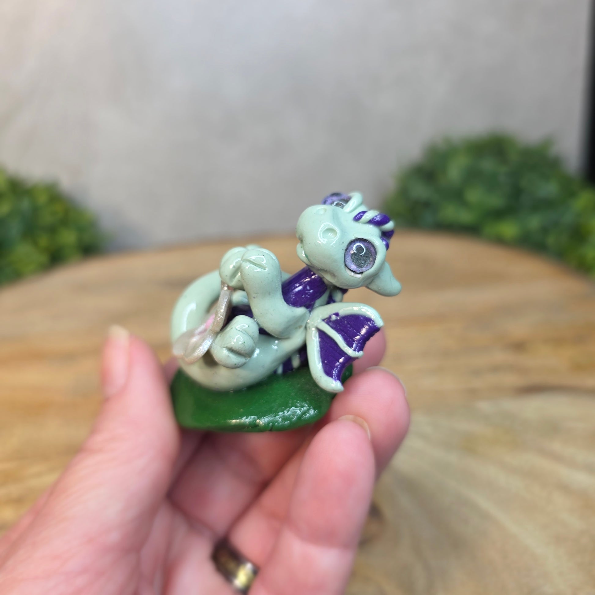 Hand holding a small green and purple creature figurine with blurred background