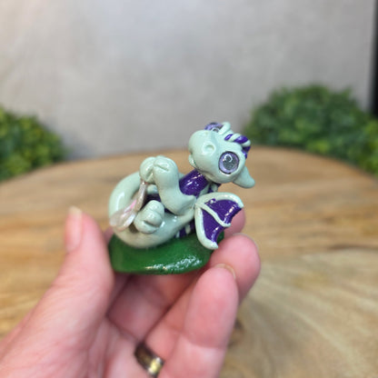 Hand holding a small green and purple creature figurine with blurred background