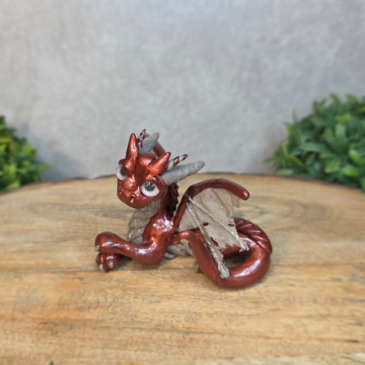 A bronze and gray clay dragon against a blurred wood surface
