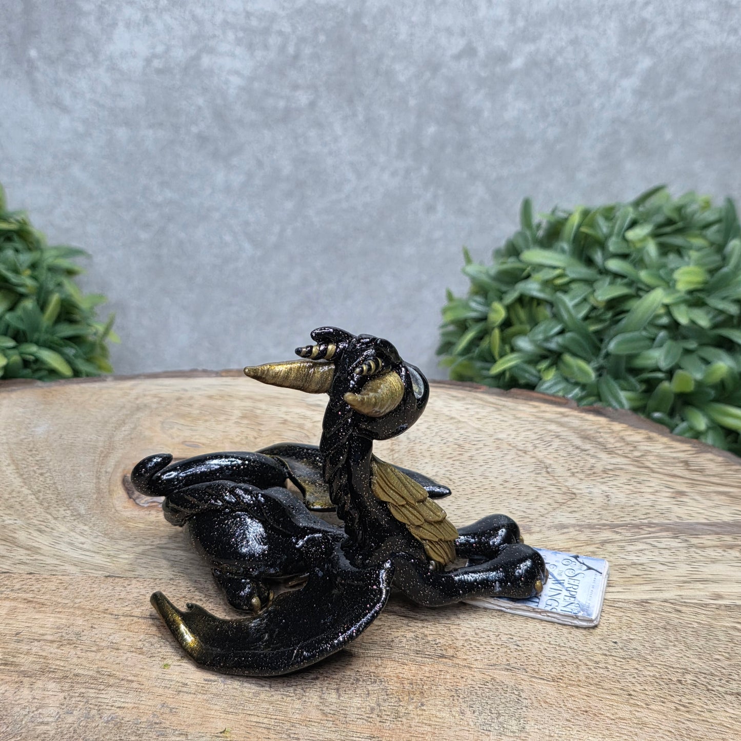 A dragon reading a book against a wood surface with greenery