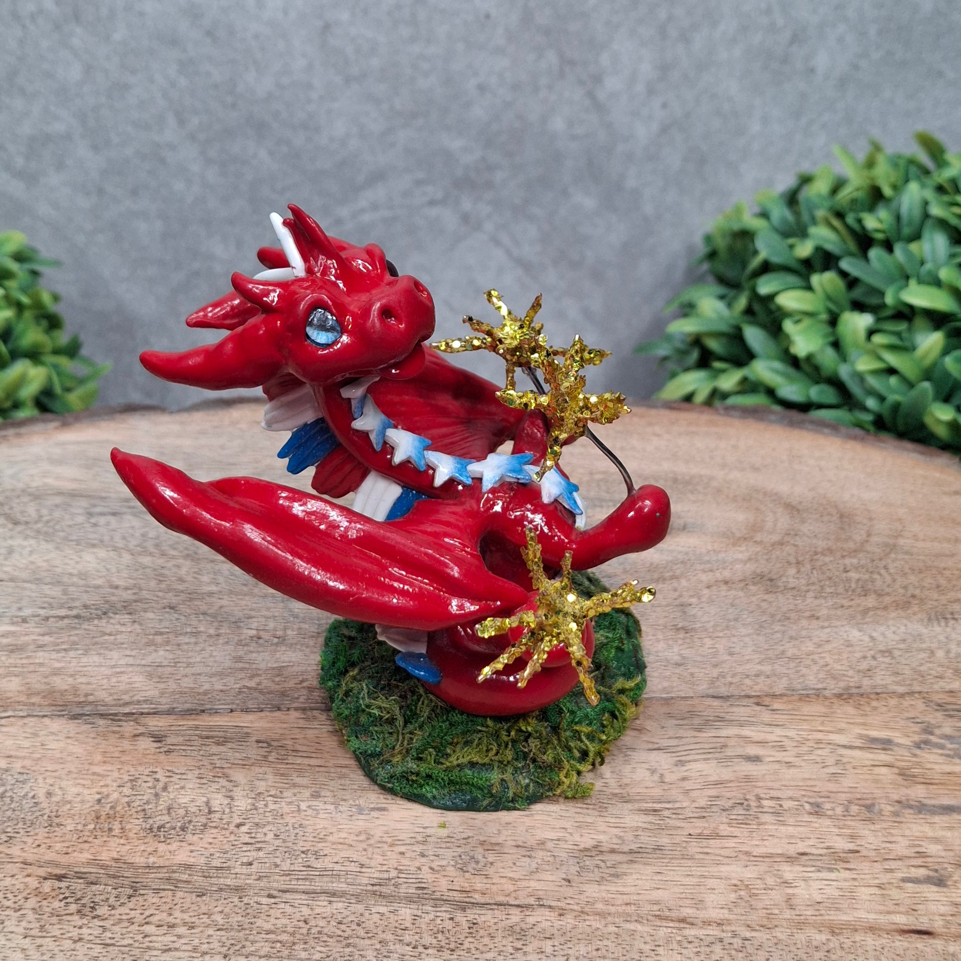 A clay dragon with sparklers against a wood surface with greenery