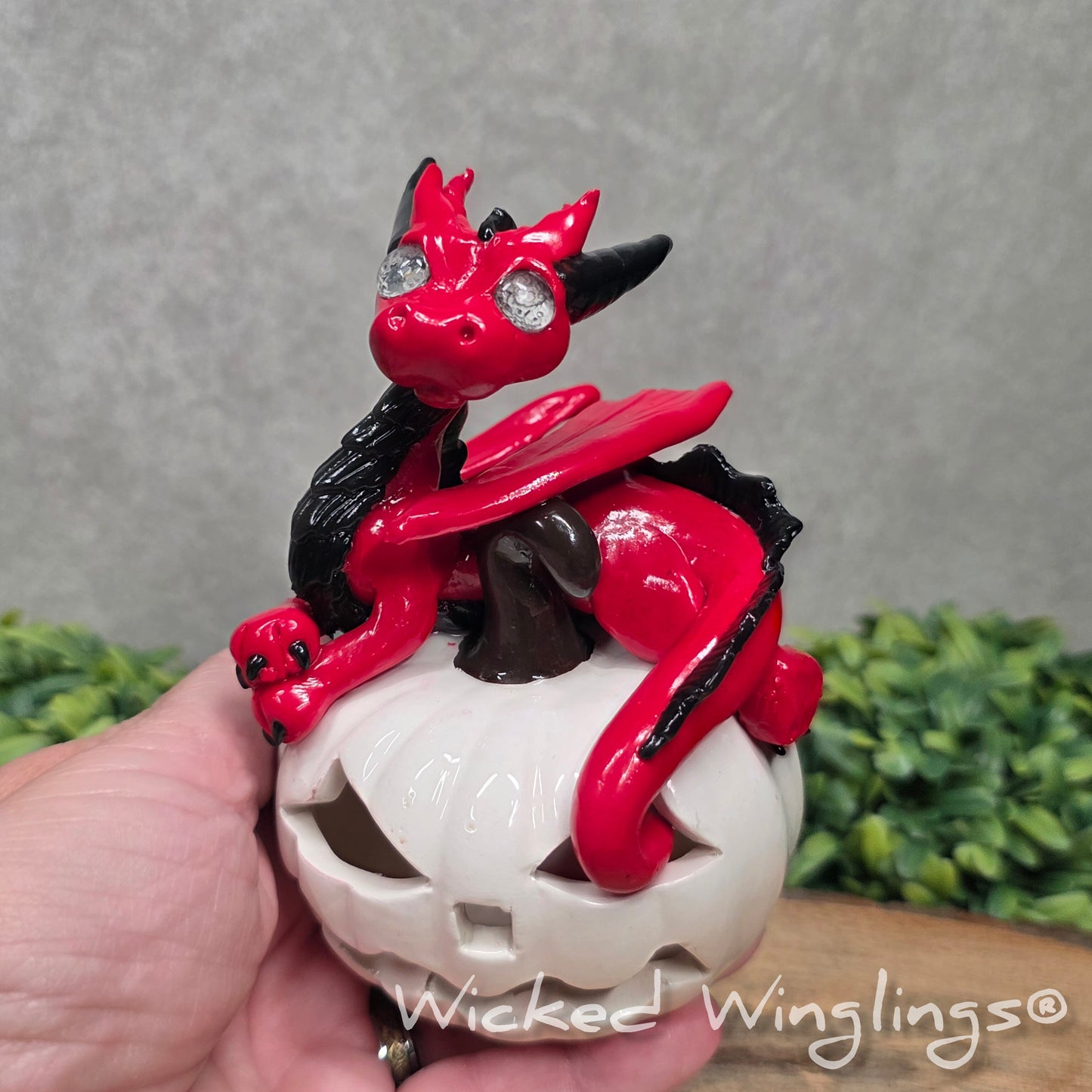 A hand holding a red dragon on a white jack o lantern