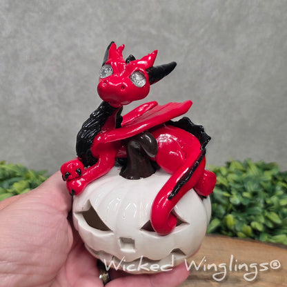 A hand holding a red dragon on a white jack o lantern