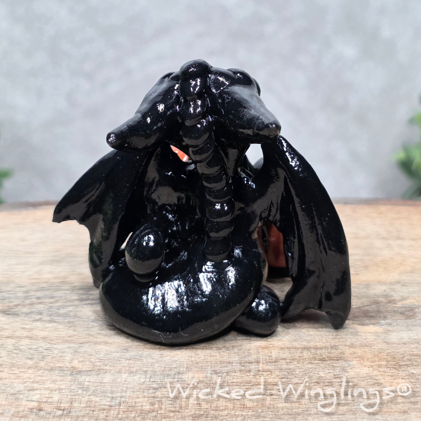 A baby clay dragon sculpture with pumpkins against a wood background with greenery and text Wicked Winglings