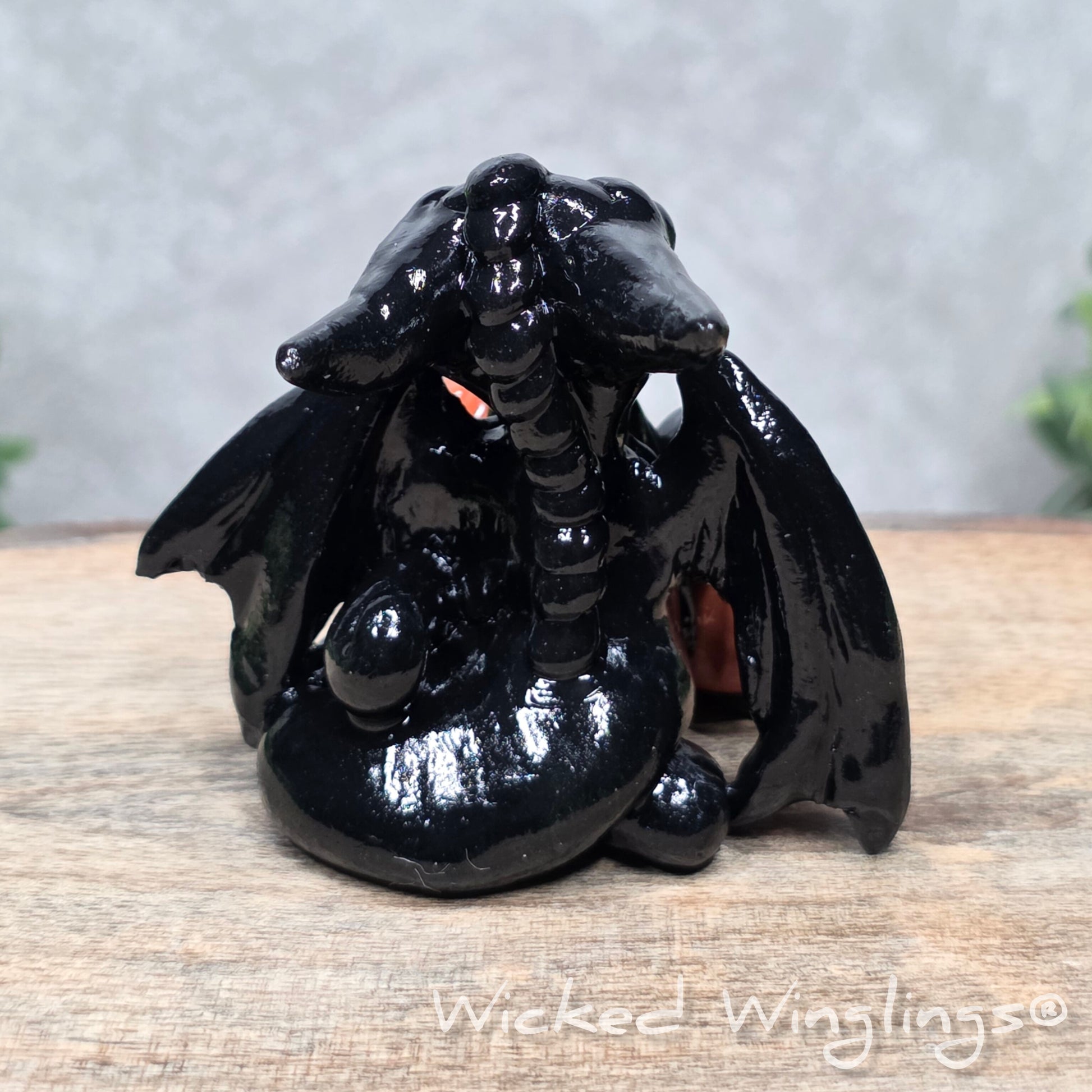 A baby clay dragon sculpture with pumpkins against a wood background with greenery and text Wicked Winglings