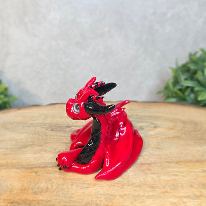 A red and black clay dragon against a blurred wood surface