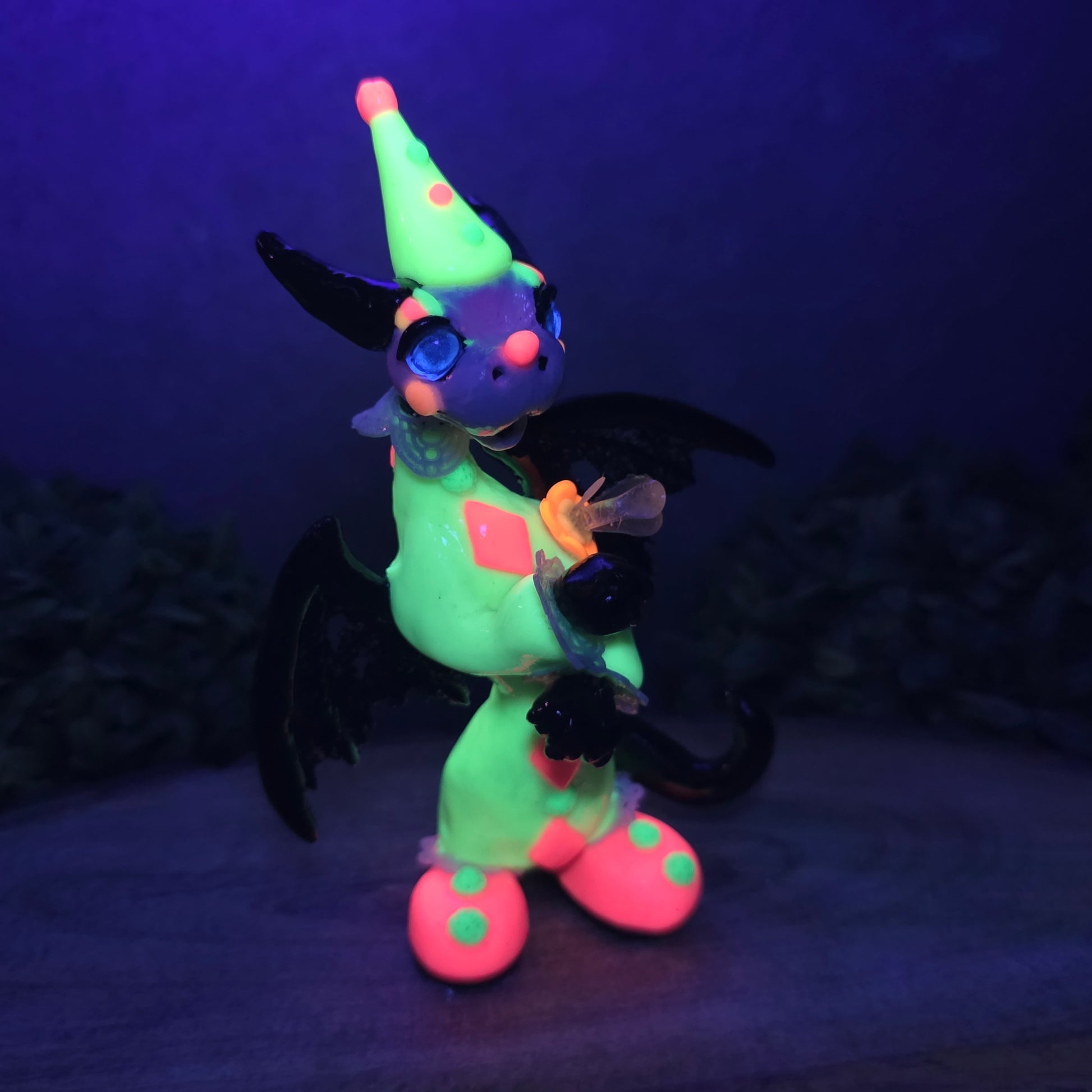 A blacklight reactive clown dragon on wood surface with greenery
